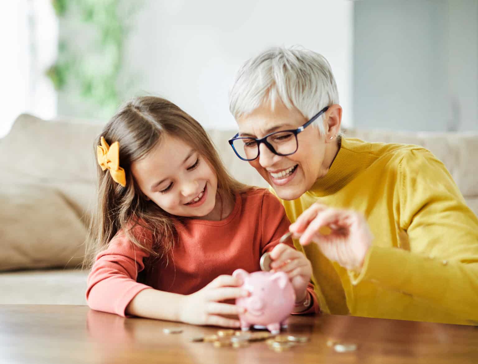 Kind und Oma stecken gemeinsam Geld in ein Sparschwein.